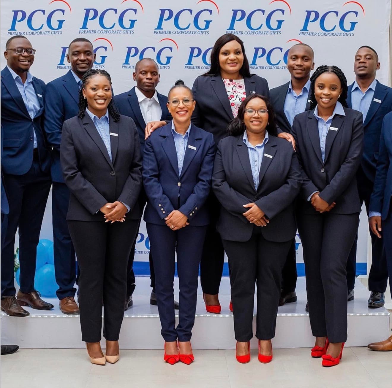 Premier Corporate Gifts team in navy corporate attire posed together in front of a branded PCG backdrop