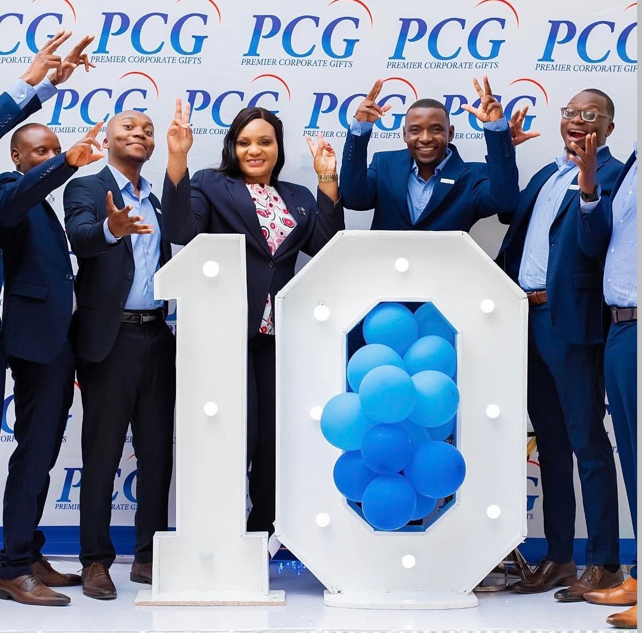 Premier Corporate Gifts team celebrating around a large illuminated number display filled with blue balloons